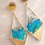 Orecchini pendenti con forma rombo/triangolare irregolare, petali di nigella blu, resina UV, stile boho elegante, 5x3 cm.