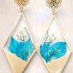 Orecchini pendenti con forma rombo/triangolare irregolare, petali di nigella blu, resina UV, stile boho elegante, 5x3 cm.