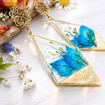 Orecchini pendenti con forma rombo/triangolare irregolare, petali di nigella blu, resina UV, stile boho elegante, 5x3 cm.