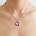 Può includere: Una collana color argento con un ciondolo a forma di cuore. Il ciondolo presenta un fiore blu e giallo racchiuso in resina trasparente. La collana è indossata intorno al collo.